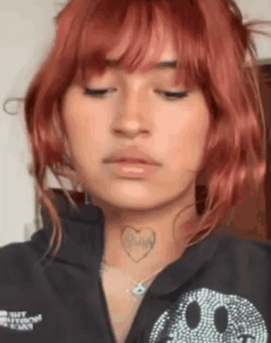 a woman with red hair and a heart tattoo on her neck is wearing a black shirt with a smiley face on it .