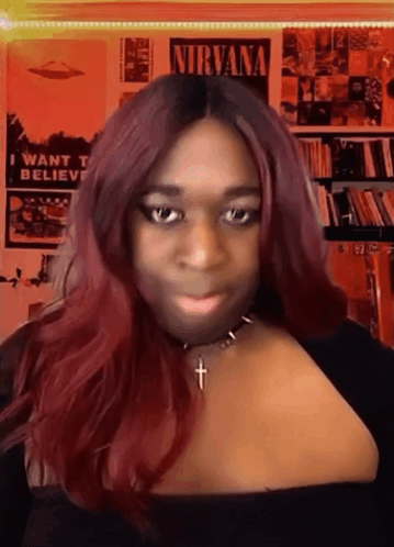 A Woman With Red Hair And A Necklace With A Cross In Front Of A Nirvana Poster GIF