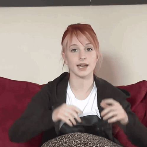 A Woman With Red Hair And A Nose Ring Is Sitting On A Couch GIF