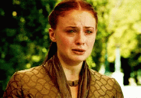 A Woman With Red Hair And A Scarf Around Her Neck Is Crying . GIF