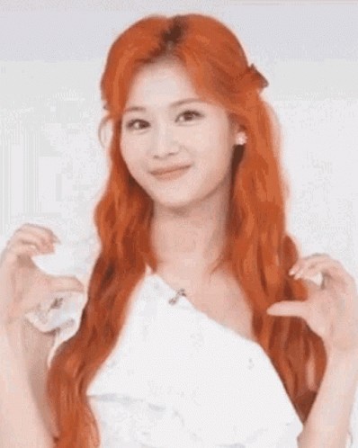 A Woman With Red Hair And A White Dress Is Making A Heart Shape With Her Hands . GIF