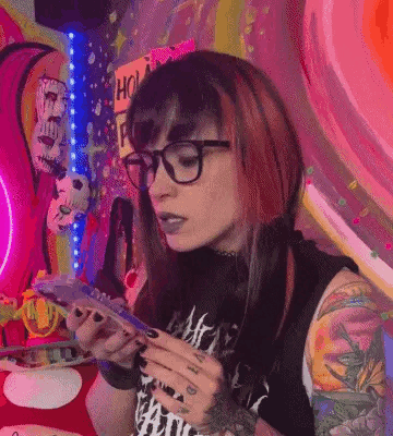A Woman With Red Hair And Glasses Is Sitting At A Table Holding A Cell Phone . GIF