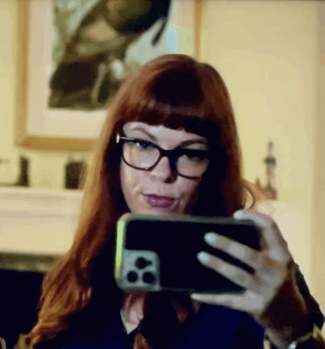 A Woman With Red Hair And Glasses Is Taking A Selfie With Her Cell Phone GIF