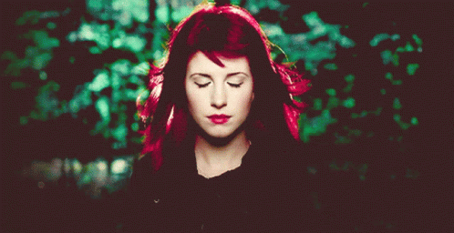 A Woman With Red Hair Has Her Eyes Closed In Front Of A Green Background GIF
