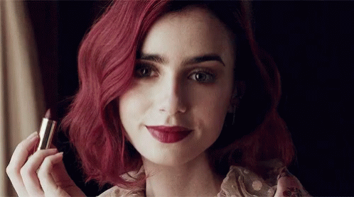 A Woman With Red Hair Holds A Lipstick In Her Hand GIF
