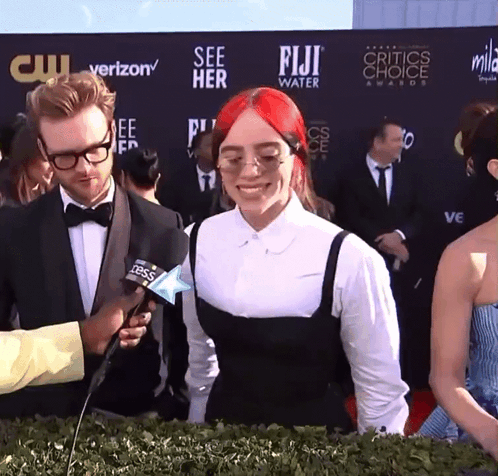 A Woman With Red Hair Is Being Interviewed By A Man In Front Of A Wall That Says Fiji Water GIF