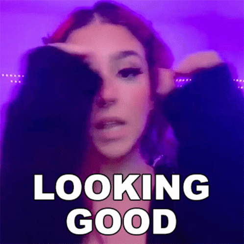 A Woman With Red Hair Is Covering Her Face With Her Hand And The Words `` Looking Good '' Written Above Her . GIF