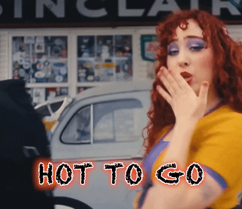 A Woman With Red Hair Is Covering Her Mouth With Her Hand And The Words Hot To Go Are Behind Her GIF