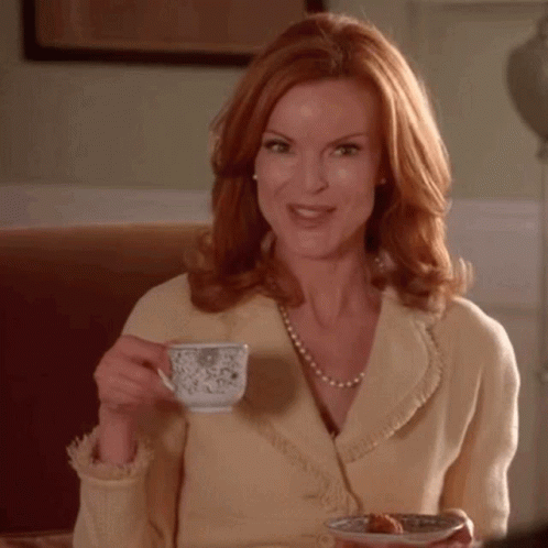 A Woman With Red Hair Is Drinking A Cup Of Tea And Holding A Plate Of Food GIF