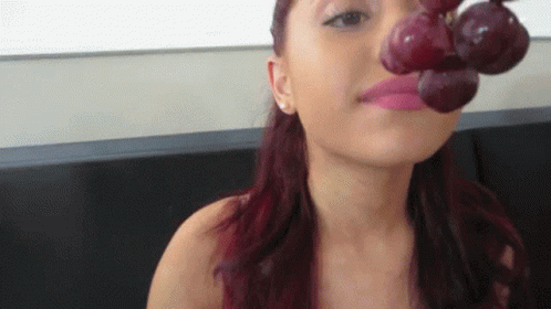 A Woman With Red Hair Is Holding A Bunch Of Grapes To Her Mouth GIF