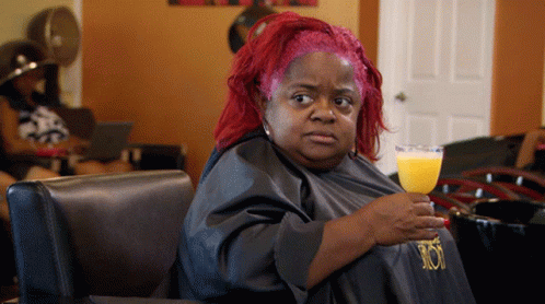 A Woman With Red Hair Is Holding A Glass Of Orange Juice In A Salon GIF