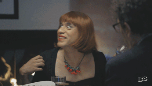 A Woman With Red Hair Is Holding A Glass Of Wine And Smiling GIF