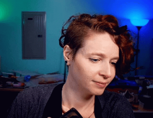 A Woman With Red Hair Is Holding A Phone In Her Hand GIF