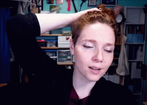 A Woman With Red Hair Is Holding Her Hair In A Messy Bun GIF