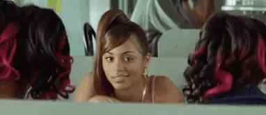A Woman With Red Hair Is Looking At Herself In The Mirror . GIF