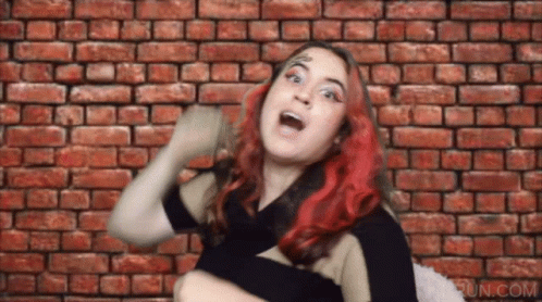 A Woman With Red Hair Is Making A Funny Face In Front Of A Brick Wall .. GIF