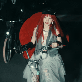 A Woman With Red Hair Is Riding A Bicycle In The Dark GIF