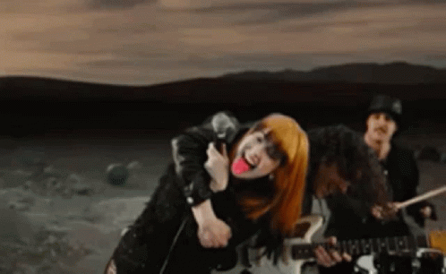 A Woman With Red Hair Is Singing Into A Microphone While A Man Plays Drums . GIF
