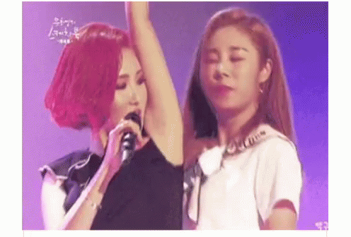A Woman With Red Hair Is Singing Into A Microphone While Another Woman Holds Her Arm Up . GIF