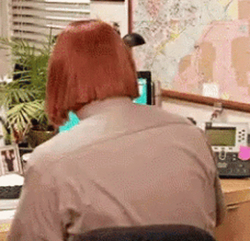 A Woman With Red Hair Is Sitting At A Desk With A Telephone And A Map On The Wall . GIF