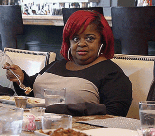 A Woman With Red Hair Is Sitting At A Table Eating GIF