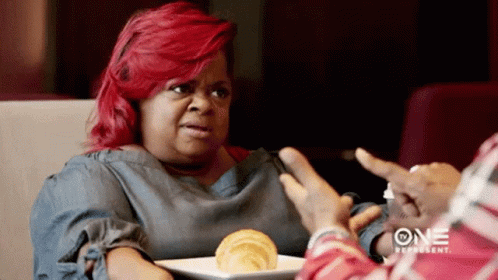 A Woman With Red Hair Is Sitting At A Table With A Plate Of Food In Front Of Her . GIF