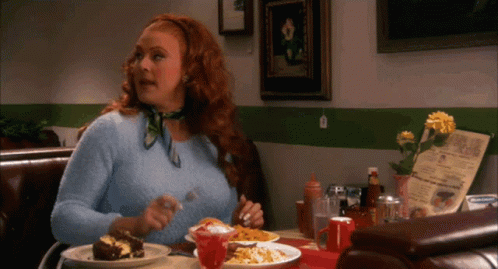 A Woman With Red Hair Is Sitting At A Table With Plates Of Food And A Menu GIF