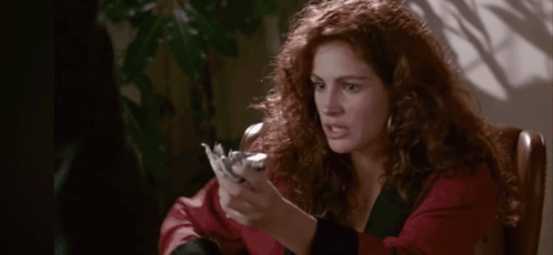 A Woman With Red Hair Is Sitting In A Chair Holding A Piece Of Paper In Her Hand . GIF