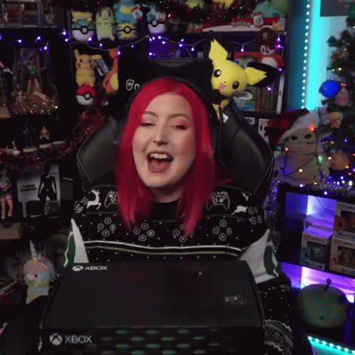 A Woman With Red Hair Is Sitting In A Gaming Chair Holding An Xbox Box GIF
