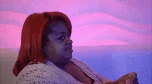 A Woman With Red Hair Is Sitting On A Couch In Front Of A Pink And Blue Background . GIF