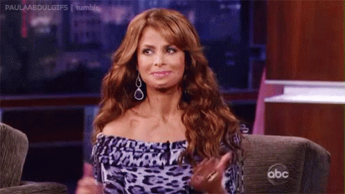 A Woman With Red Hair Is Sitting On A Couch With Her Hands In The Air . GIF
