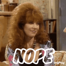 A Woman With Red Hair Is Sitting On A Couch With The Word Nope Written In White Letters . GIF
