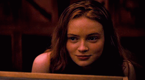 A Woman With Red Hair Is Smiling And Looking At The Camera GIF