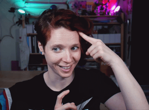 A Woman With Red Hair Is Smiling And Pointing At Her Head GIF