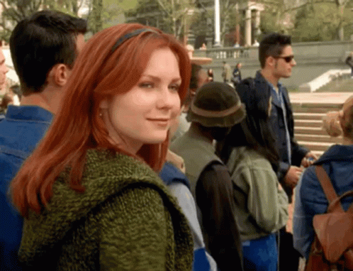 A Woman With Red Hair Is Smiling In A Crowd GIF