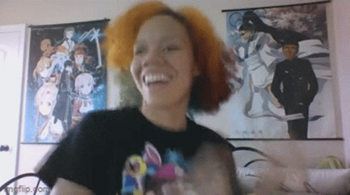 A Woman With Red Hair Is Smiling In Front Of Anime Posters On The Wall GIF