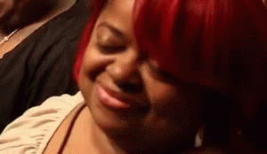 A Woman With Red Hair Is Smiling With Her Eyes Closed And Making A Funny Face . GIF