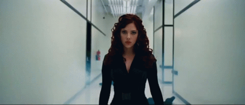 A Woman With Red Hair Is Standing In A Hallway And Looking At The Camera GIF