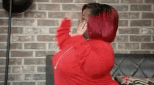 A Woman With Red Hair Is Standing In Front Of A Brick Wall And Covering Her Face With Her Hands . GIF