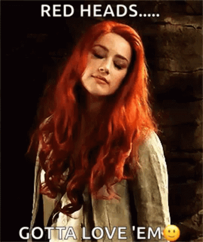 A Woman With Red Hair Is Standing In Front Of A Brick Wall With Her Eyes Closed . GIF