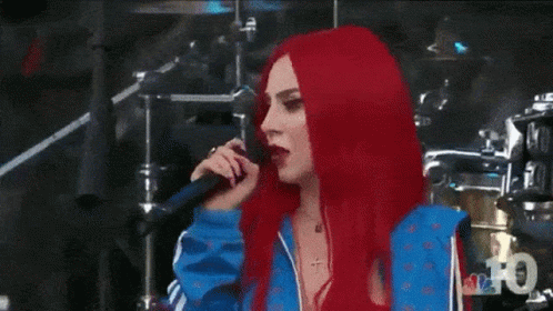 A Woman With Red Hair Is Standing In Front Of A Drum Set And Looking At The Camera . GIF
