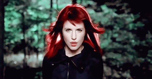 A Woman With Red Hair Is Standing In Front Of A Forest GIF