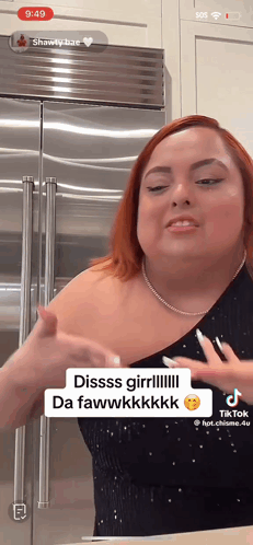 A Woman With Red Hair Is Standing In Front Of A Stainless Steel Refrigerator And Has A Tiktok App Open GIF