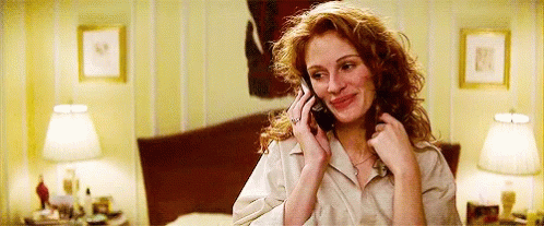 A Woman With Red Hair Is Talking On A Cell Phone In A Bedroom . GIF
