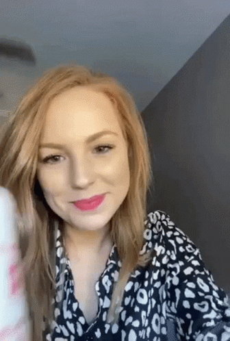 A Woman With Red Hair Is Wearing A Black And White Leopard Print Shirt And Lipstick . GIF
