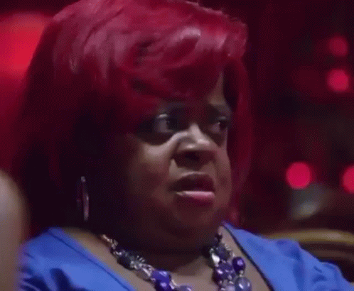 A Woman With Red Hair Is Wearing A Blue Dress And A Blue Necklace And Making A Funny Face . GIF