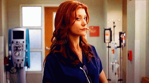 A Woman With Red Hair Is Wearing A Blue Scrub Top And Sunglasses In A Hospital Hallway . GIF