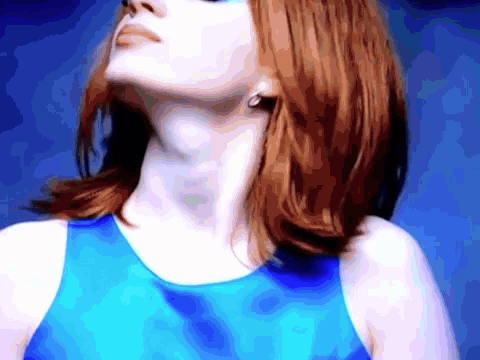 A Woman With Red Hair Is Wearing A Blue Tank Top And Earrings GIF