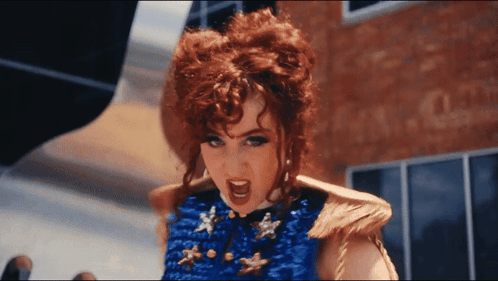 A Woman With Red Hair Is Wearing A Blue Top With Gold Stars GIF