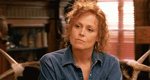 A Woman With Red Hair Is Wearing A Denim Shirt And Earrings GIF